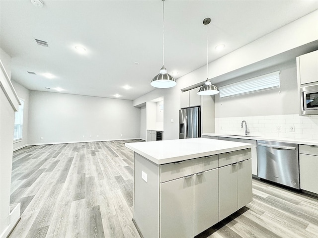 kitchen featuring a center island, sink, stainless steel appliances, pendant lighting, and light wood-type flooring