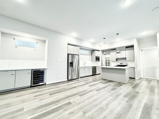 kitchen featuring appliances with stainless steel finishes, decorative light fixtures, a center island, light hardwood / wood-style floors, and wine cooler