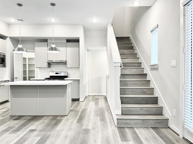 kitchen with decorative light fixtures, a kitchen island, light hardwood / wood-style flooring, and tasteful backsplash