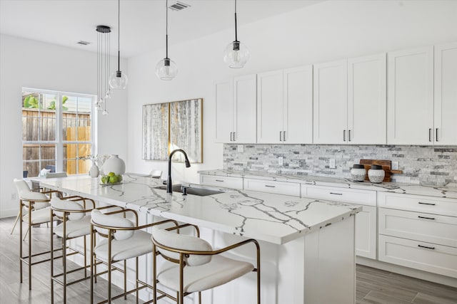 kitchen featuring white cabinetry, a kitchen island with sink, and pendant lighting