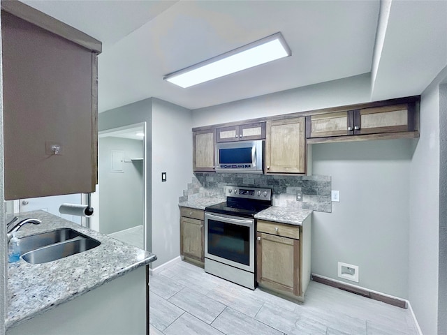 kitchen with backsplash, light stone countertops, sink, and appliances with stainless steel finishes