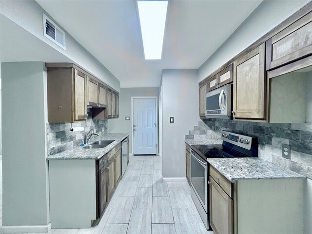 kitchen featuring sink, a skylight, light stone countertops, appliances with stainless steel finishes, and tasteful backsplash