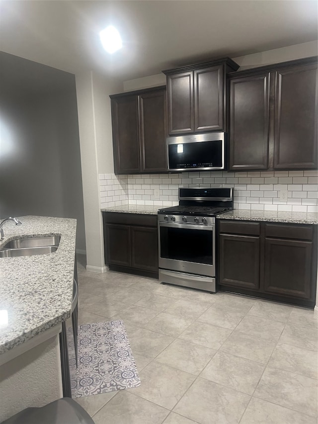 kitchen featuring decorative backsplash, light stone countertops, sink, and appliances with stainless steel finishes