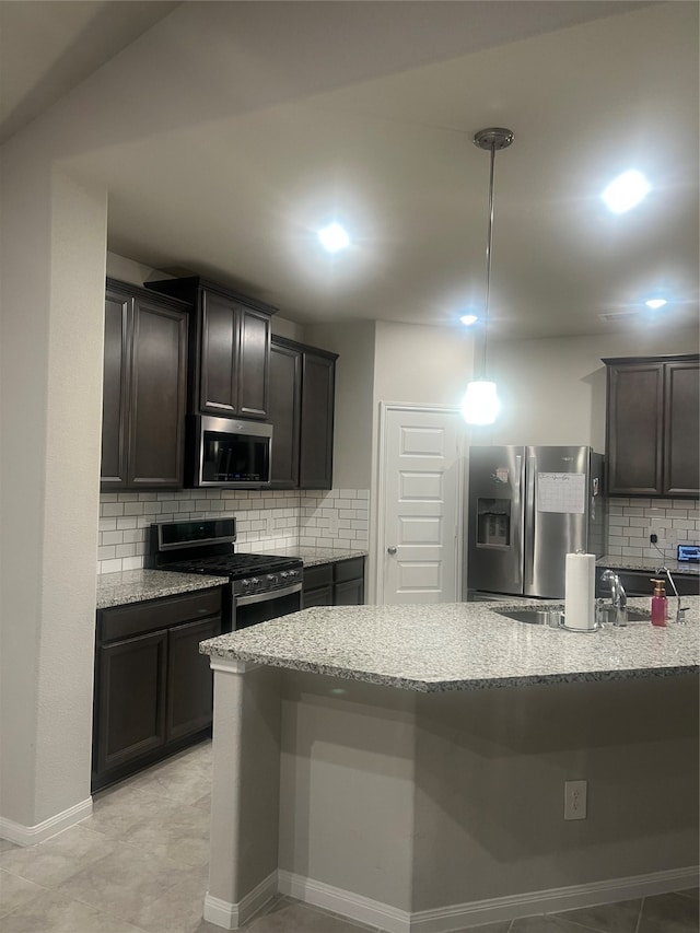 kitchen featuring dark brown cabinetry, light stone counters, backsplash, pendant lighting, and appliances with stainless steel finishes