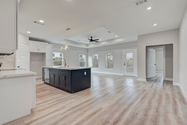 kitchen with a kitchen island with sink, ceiling fan, sink, light hardwood / wood-style flooring, and white cabinets