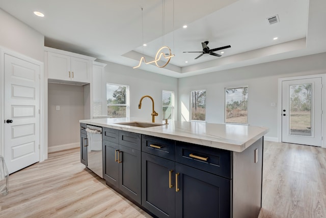 kitchen with a tray ceiling, white cabinets, sink, and an island with sink