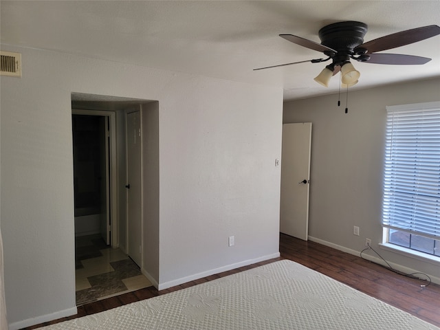 unfurnished bedroom with ceiling fan, ensuite bathroom, and dark wood-type flooring