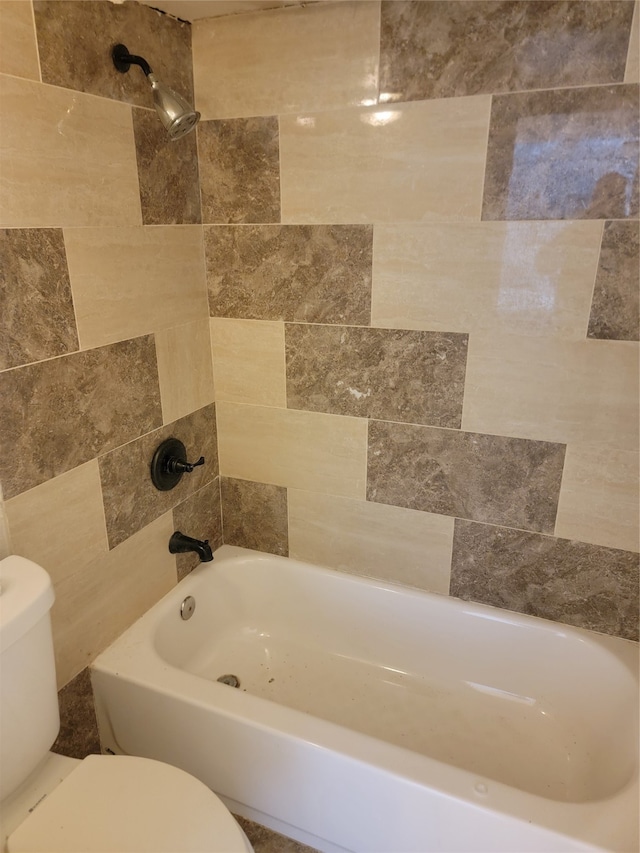 bathroom with tiled shower / bath combo, toilet, and tile walls