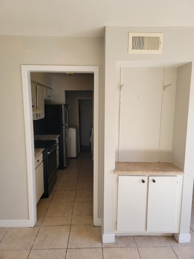 kitchen with washer / clothes dryer, black electric range, white cabinets, and light tile patterned floors