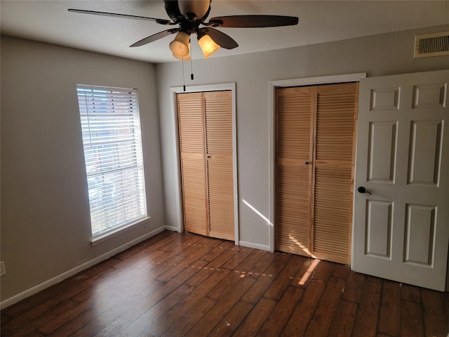 unfurnished bedroom with dark wood-type flooring, multiple windows, multiple closets, and ceiling fan