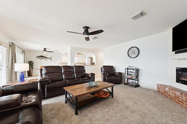 living room with ceiling fan, a fireplace, light colored carpet, and a textured ceiling