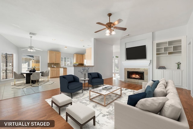 living room with ceiling fan, light hardwood / wood-style flooring, built in features, and lofted ceiling