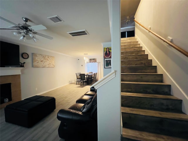 stairway featuring a fireplace, wood-type flooring, and ceiling fan