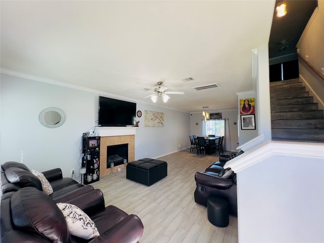 living room with a tiled fireplace, crown molding, ceiling fan, and light wood-type flooring