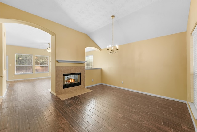 unfurnished living room featuring ceiling fan with notable chandelier, lofted ceiling, dark wood-type flooring, and a tile fireplace