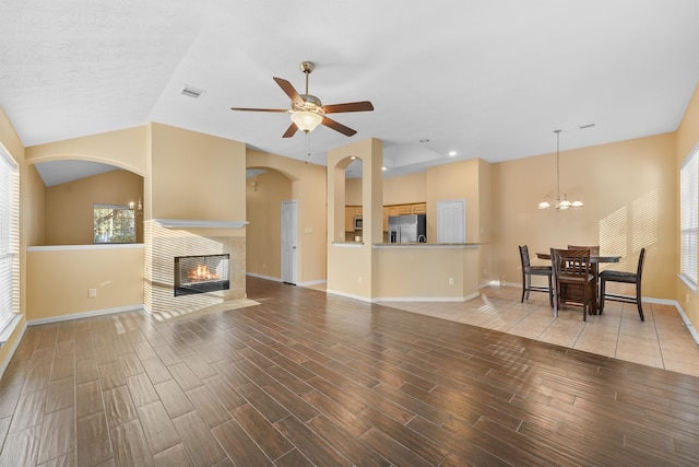 tiled living room featuring ceiling fan with notable chandelier, lofted ceiling, and a fireplace