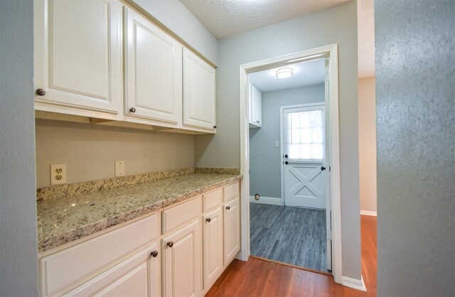 bar with light stone counters, white cabinets, dark wood-type flooring, and a textured ceiling