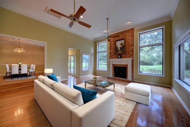 living room with ceiling fan with notable chandelier, crown molding, light wood-type flooring, a fireplace, and a towering ceiling