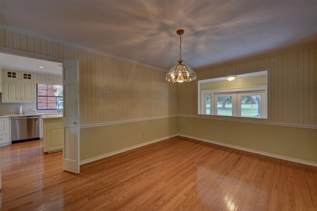 spare room featuring a chandelier, light wood-type flooring, and ornamental molding