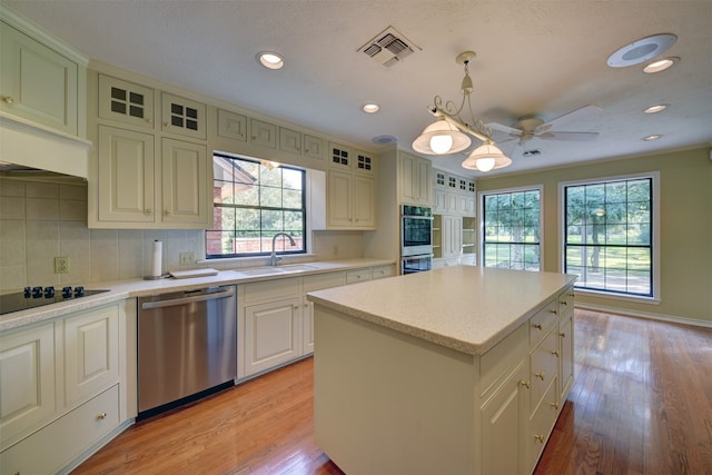 kitchen with appliances with stainless steel finishes, sink, pendant lighting, light hardwood / wood-style flooring, and a center island