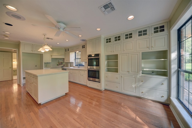 kitchen featuring plenty of natural light, a kitchen island, hanging light fixtures, and light hardwood / wood-style flooring