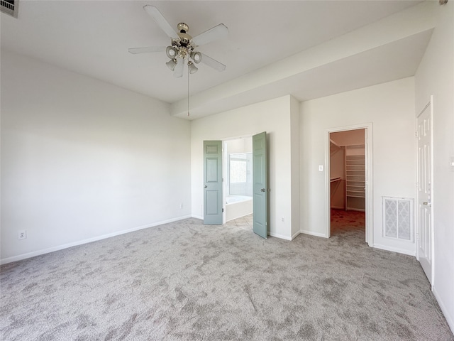 unfurnished bedroom featuring light colored carpet, ceiling fan, a spacious closet, connected bathroom, and a closet