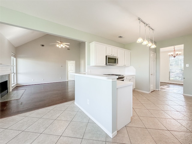 kitchen featuring light hardwood / wood-style floors, vaulted ceiling, a tiled fireplace, white cabinets, and appliances with stainless steel finishes