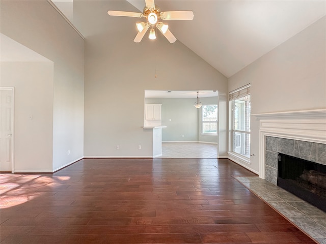 unfurnished living room with ceiling fan, dark hardwood / wood-style flooring, a tile fireplace, and high vaulted ceiling