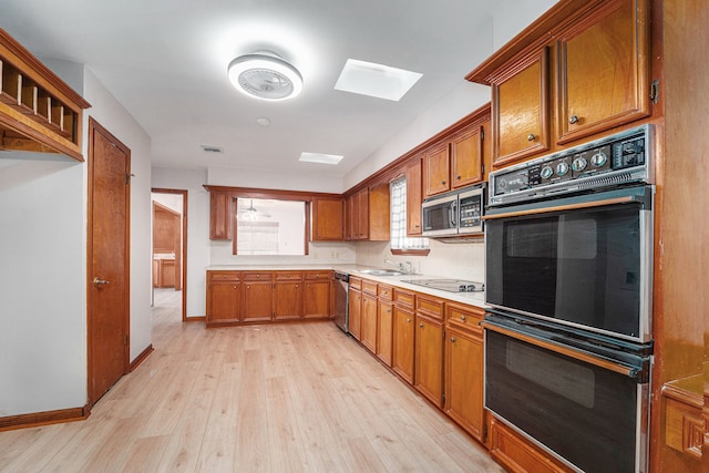 kitchen featuring appliances with stainless steel finishes, a skylight, light hardwood / wood-style flooring, and sink