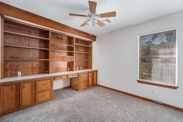 unfurnished office with light carpet, ceiling fan, and built in desk