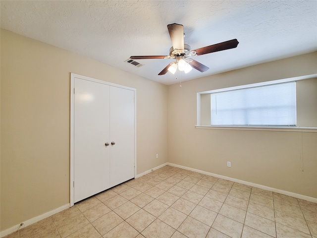 unfurnished bedroom with ceiling fan, light tile patterned floors, a textured ceiling, and a closet