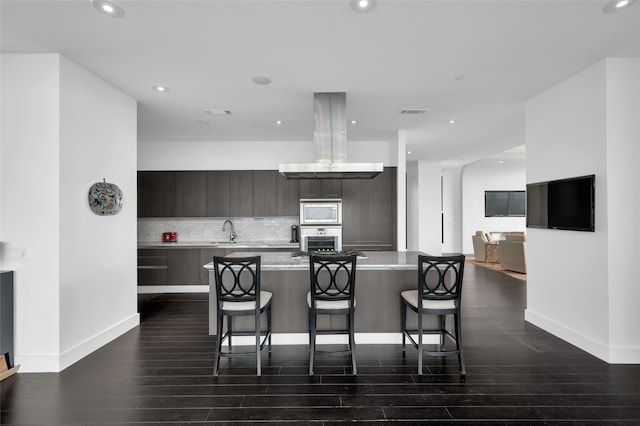 kitchen featuring island exhaust hood, a kitchen bar, stainless steel appliances, sink, and dark hardwood / wood-style floors