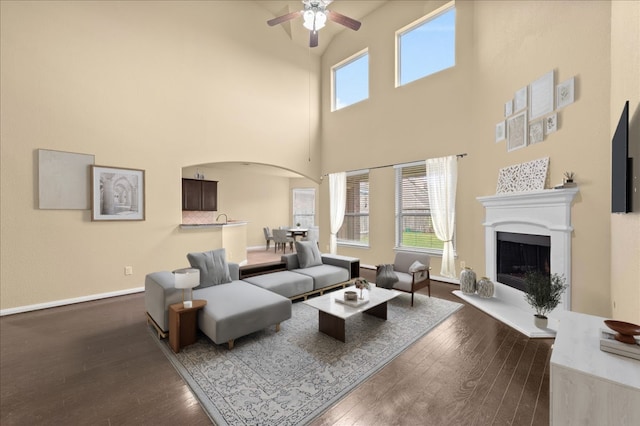 living room featuring ceiling fan, dark hardwood / wood-style flooring, a healthy amount of sunlight, and a high ceiling