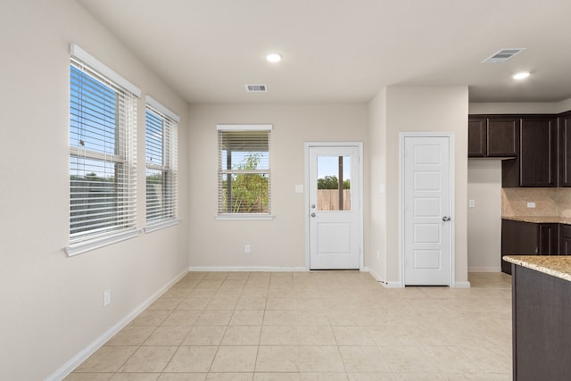 kitchen with backsplash, light stone counters, dark brown cabinets, and light tile patterned floors