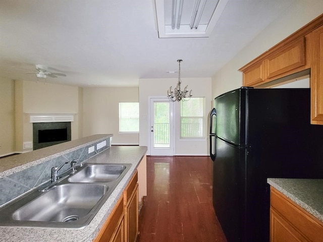 kitchen featuring ceiling fan with notable chandelier, black refrigerator, hanging light fixtures, sink, and dark hardwood / wood-style floors