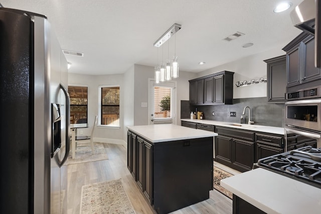 kitchen with sink, light wood-type flooring, tasteful backsplash, a kitchen island, and stainless steel appliances