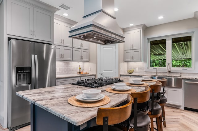 kitchen featuring light stone countertops, stainless steel appliances, tasteful backsplash, a kitchen island, and custom exhaust hood