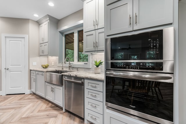 kitchen featuring light stone countertops, sink, backsplash, light parquet flooring, and appliances with stainless steel finishes