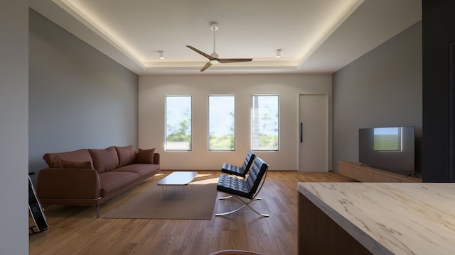 living room featuring a raised ceiling, ceiling fan, and light hardwood / wood-style floors