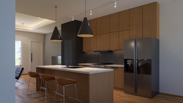 kitchen with black fridge, light hardwood / wood-style flooring, a kitchen island with sink, and sink