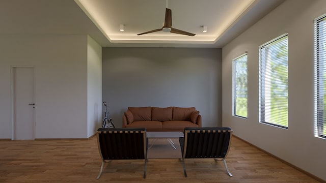 living area with light wood-type flooring, a raised ceiling, and ceiling fan