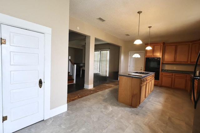 kitchen featuring pendant lighting, black double oven, a center island, a textured ceiling, and stainless steel gas stovetop