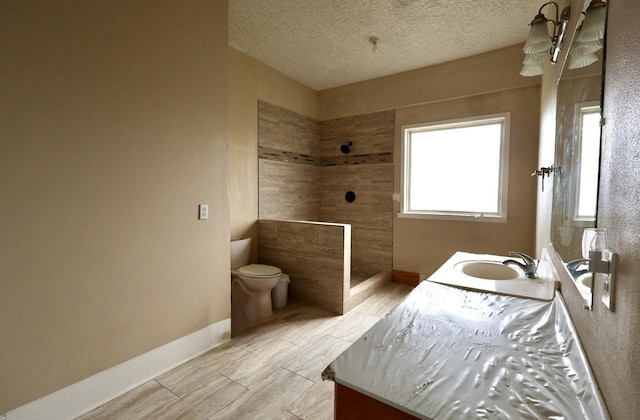 bathroom with tiled shower, vanity, toilet, and a textured ceiling