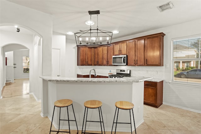 kitchen with sink, light stone countertops, appliances with stainless steel finishes, tasteful backsplash, and a chandelier