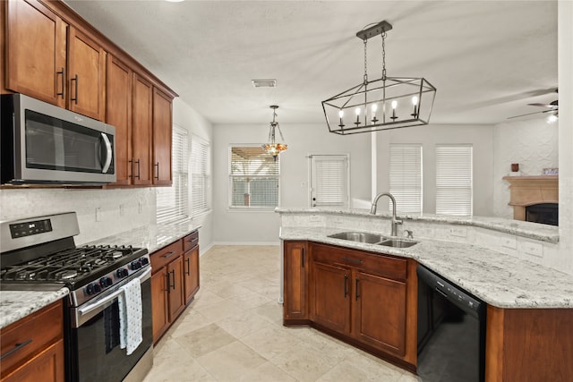 kitchen featuring light stone countertops, appliances with stainless steel finishes, ceiling fan with notable chandelier, sink, and hanging light fixtures