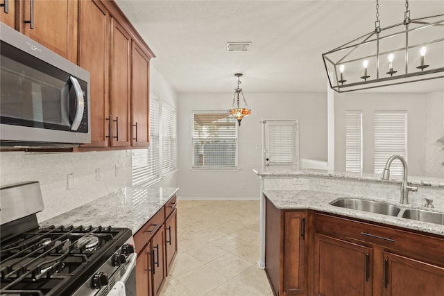 kitchen with an inviting chandelier, sink, hanging light fixtures, light stone counters, and stainless steel appliances