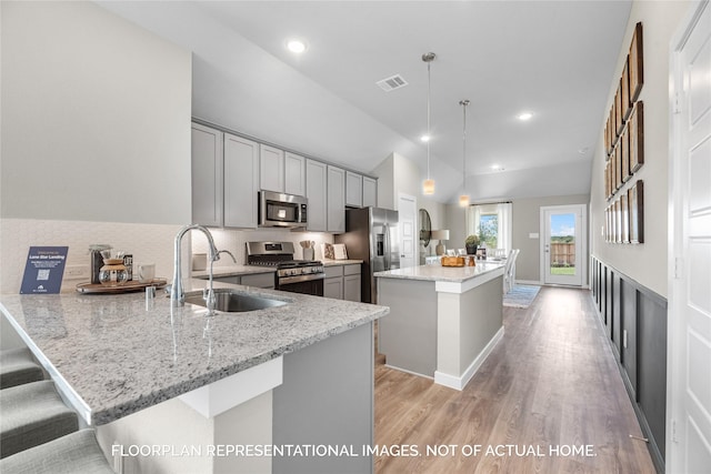 kitchen with gray cabinetry, light stone countertops, decorative light fixtures, appliances with stainless steel finishes, and light wood-type flooring