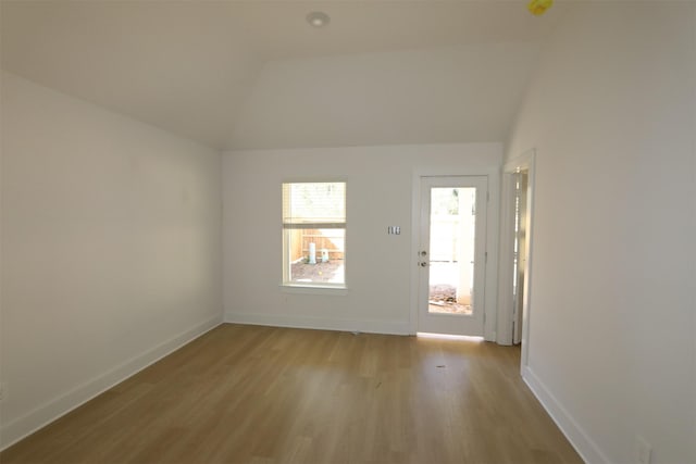 empty room with lofted ceiling, light wood-type flooring, and baseboards