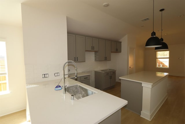 kitchen featuring lofted ceiling, visible vents, a sink, wood finished floors, and a peninsula