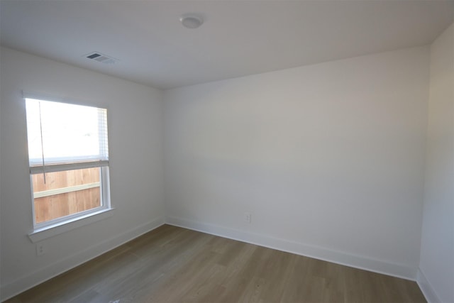 empty room with wood finished floors, visible vents, and baseboards